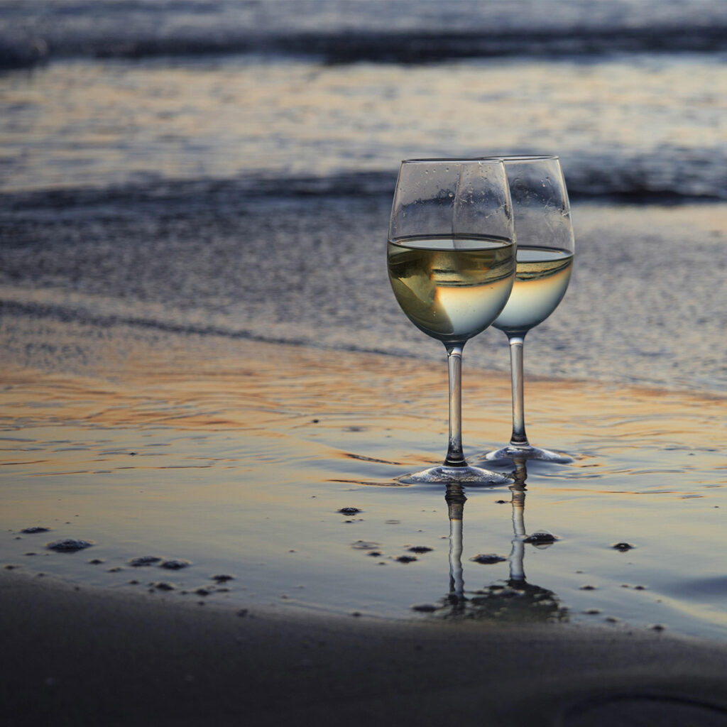 Two wine glasses in the sand reflecting a golden sunset at the beach near Casa Amorsol.