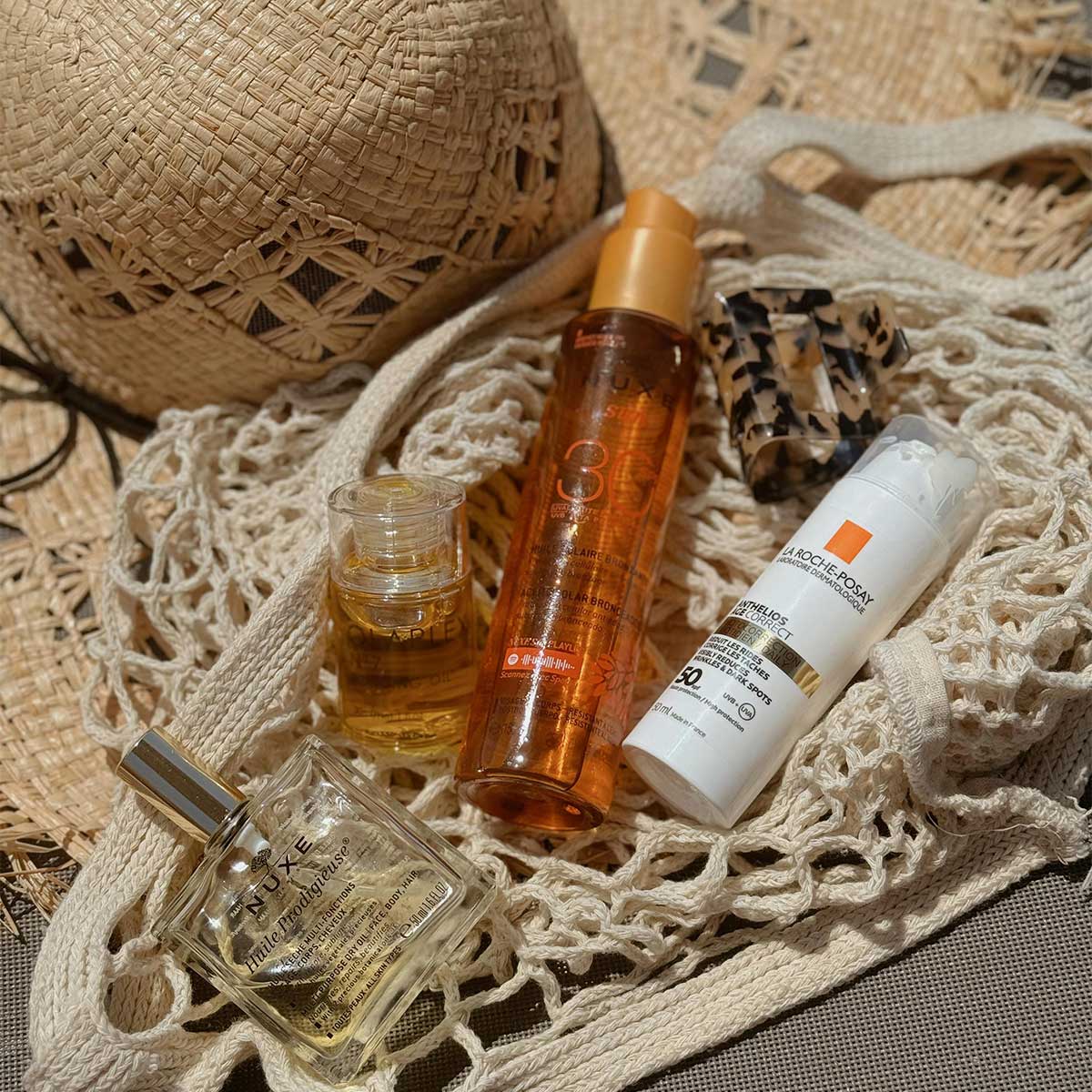 Straw hat, sunscreen, and perfume arranged in warm light — a flat lay of effortless coastal living.