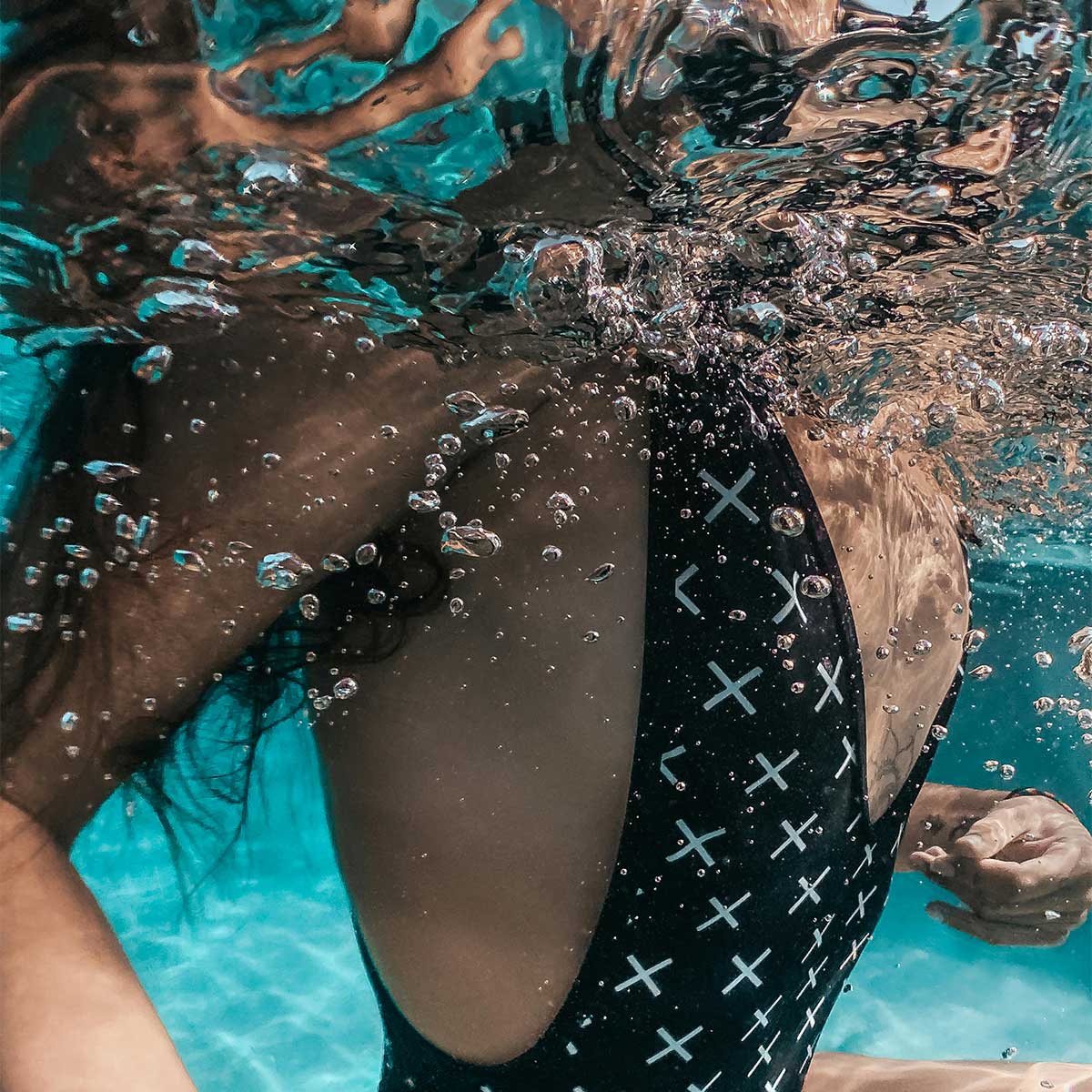 Artistic underwater shot showing swimsuit pattern and air bubbles in clear water.