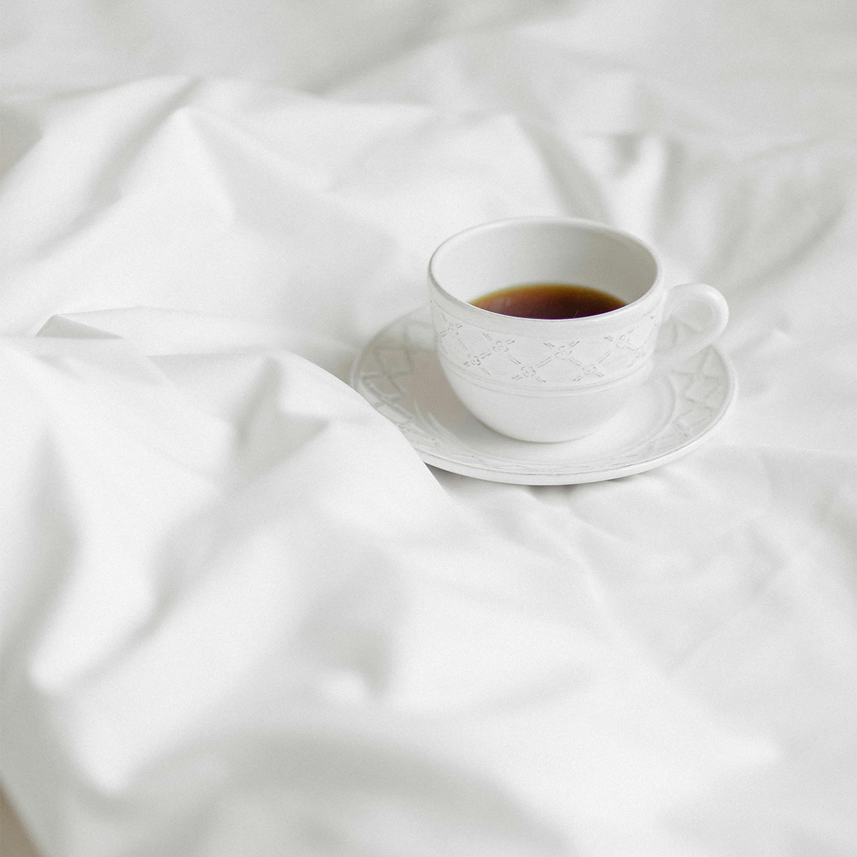 White porcelain cup on soft white bedding — the simplicity of a peaceful morning.