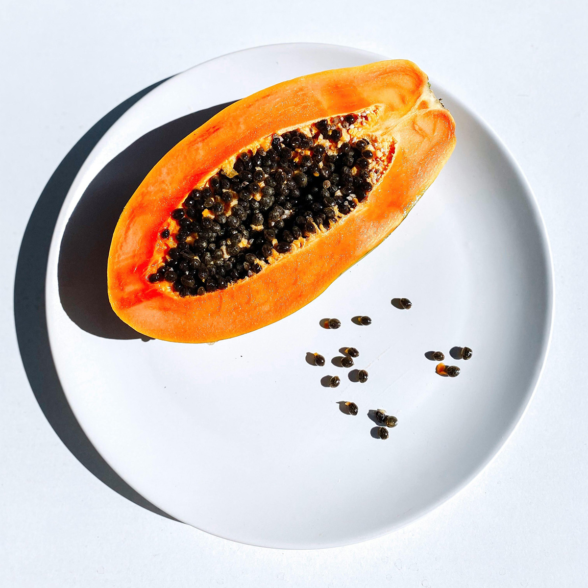 Fresh papaya with seeds on a white plate — tropical fruit captured in natural light.