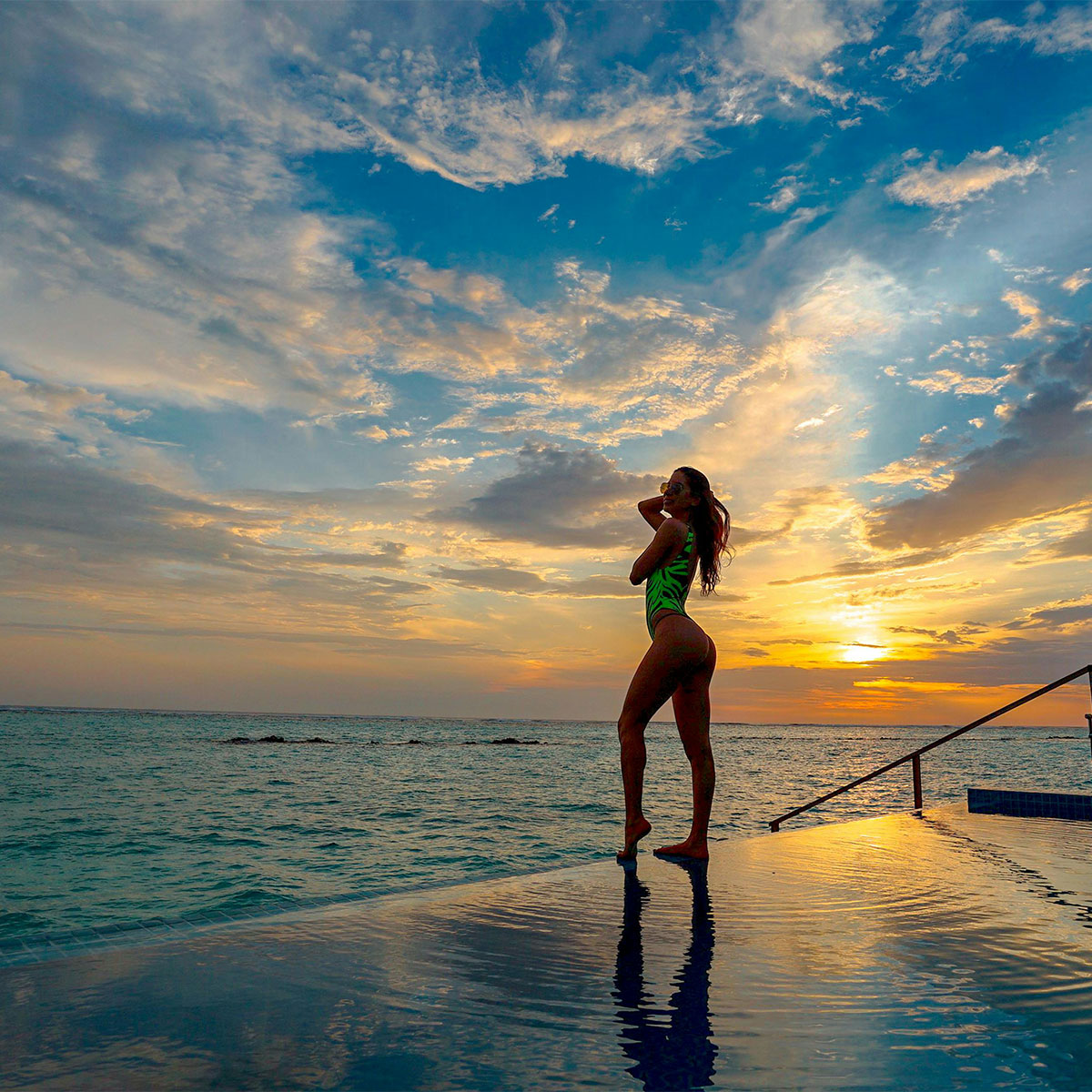 Woman at infinity pool during golden hour — serene luxury with ocean view.