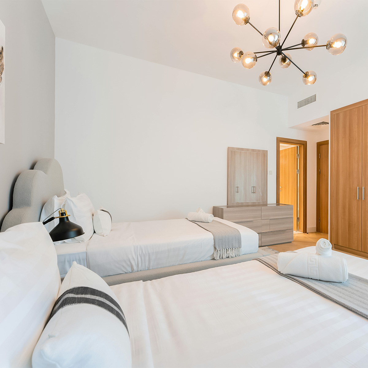 Bright and airy guest bedroom at Casa Amorsol with twin beds, warm wood accents, and minimalist décor reflecting modern coastal design and serene comfort.