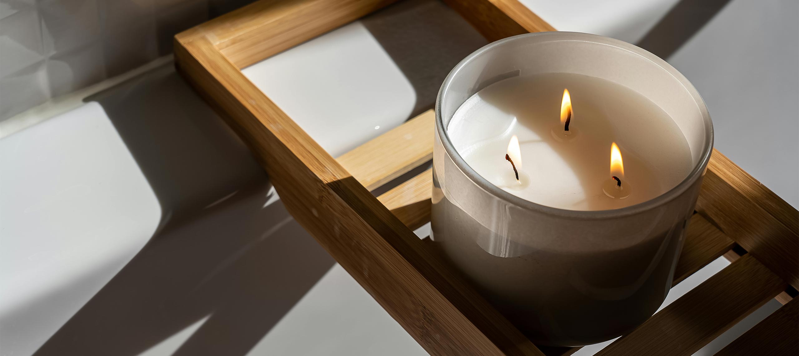 Close-up of a lit candle on a wooden bath tray beside a white tub, sunlight reflecting softly — symbolizing relaxation, calm, and the serene atmosphere of a coastal villa.
