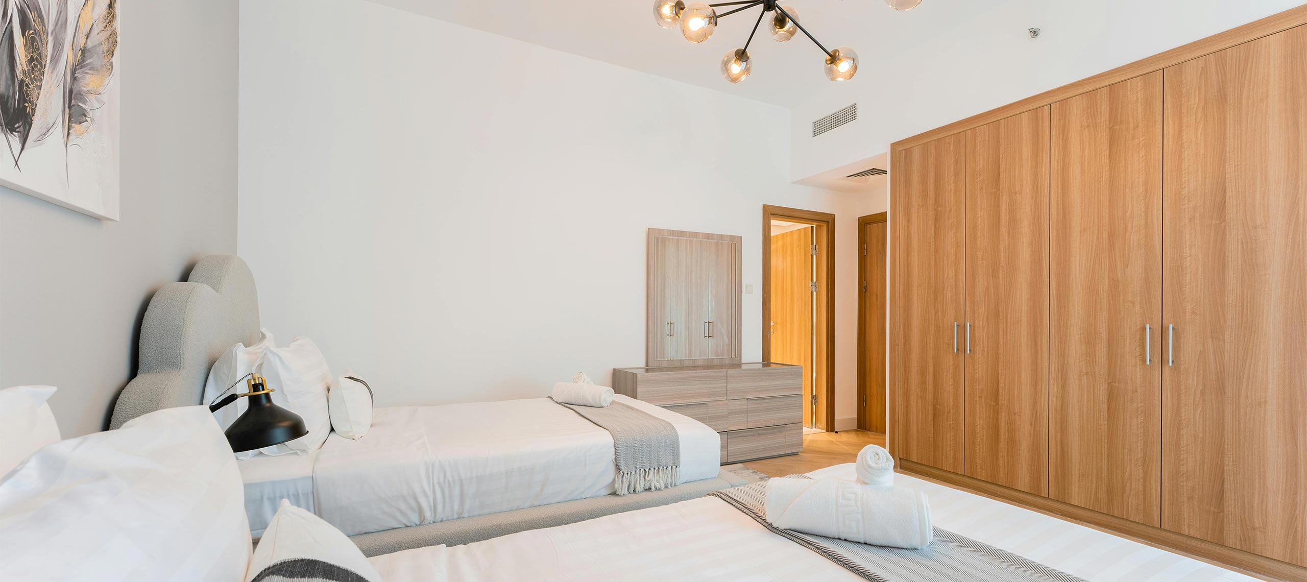 Spacious master bedroom with king bed, warm wood accents, modern lighting, and minimalist artwork — coastal villa interior with elegant, contemporary style.