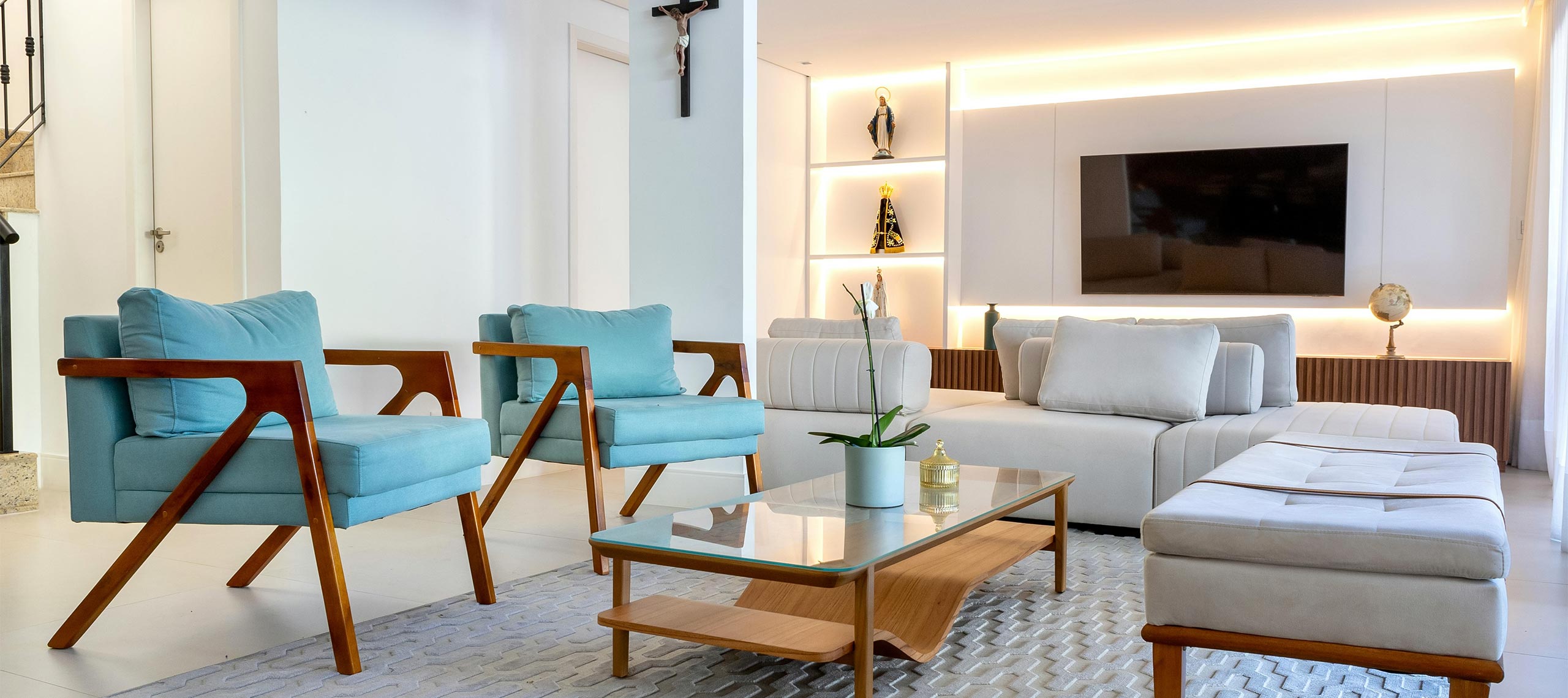 Modern villa living room with light blue armchairs, white sofa, wooden furniture, and warm ambient lighting — a cozy, coastal-inspired space to relax.