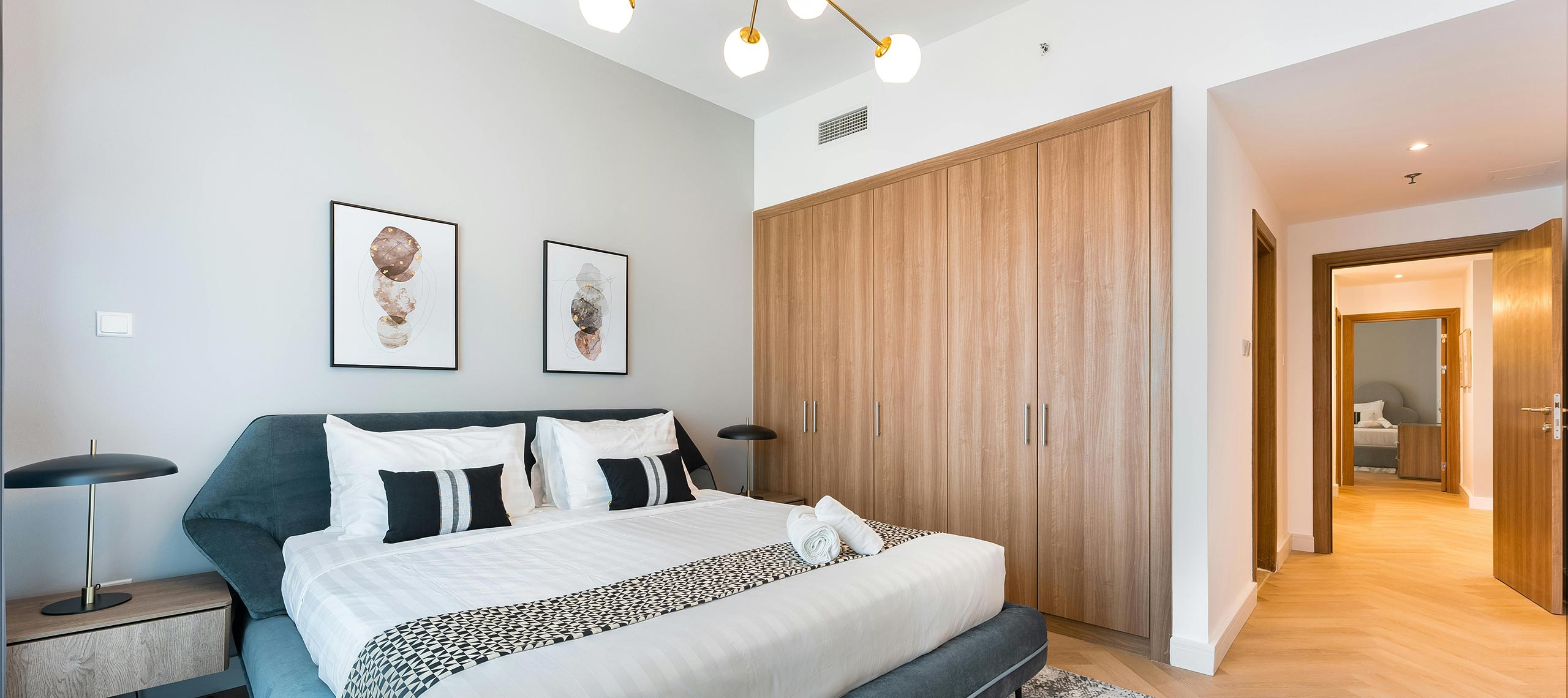 Spacious master bedroom with king bed, warm wood accents, modern lighting, and minimalist artwork — coastal villa interior with elegant, contemporary style.